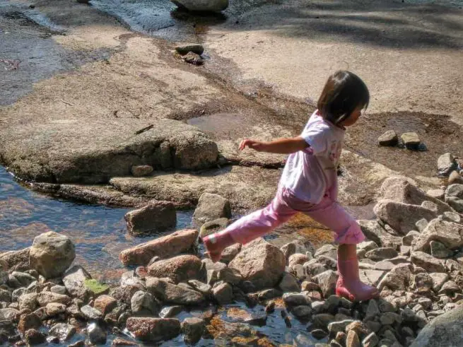 "A child skipping on stones to cross a small river in a hiking trail in Kjøsterudjuvet Drammen" 